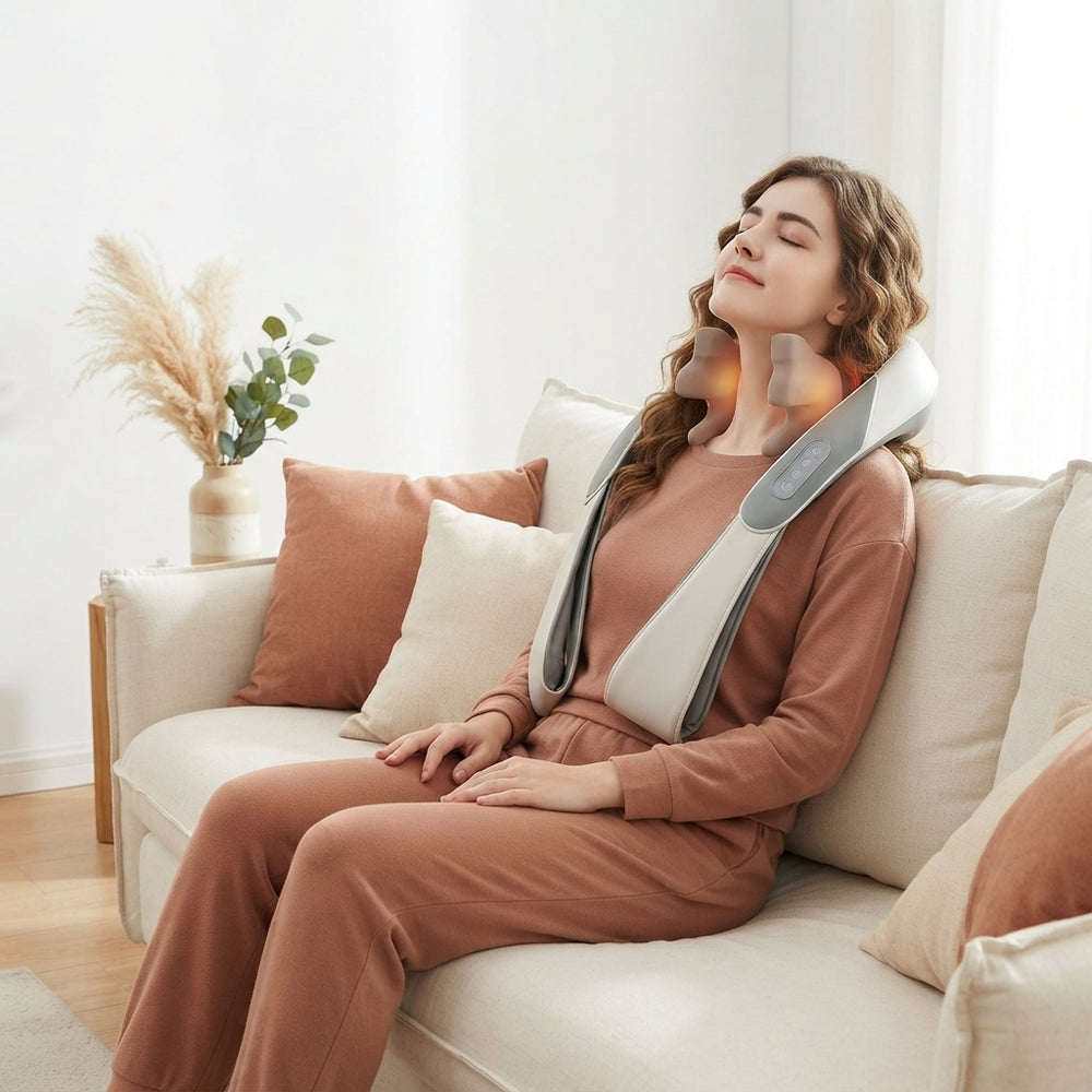 A person relaxing on a cream sofa while using a portable kneading massager on their neck and shoulders.